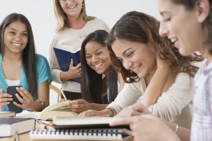 Four teenage girls studying with a teacher standing beside them