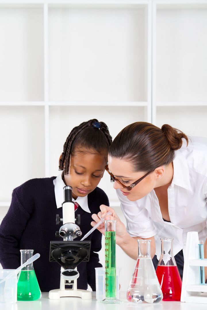 friendly teacher helping primary schoolgirl in science class