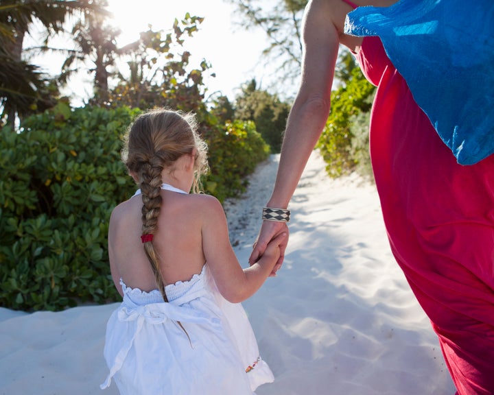 Five year old girl holding her mother's hand while walking in the sand.