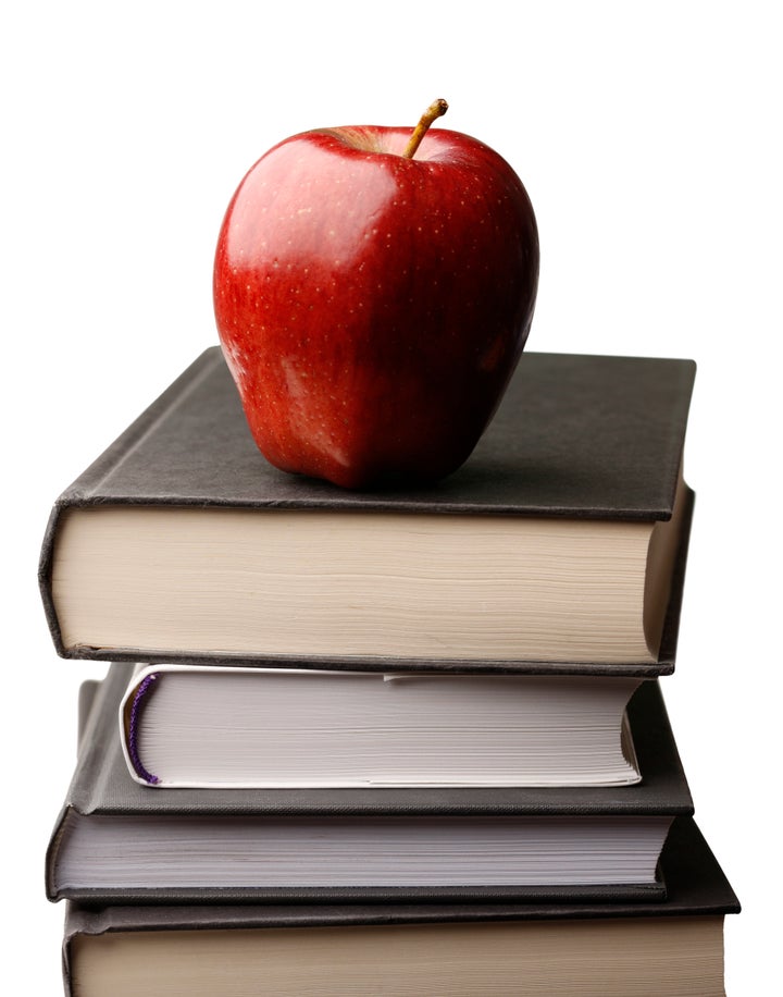 A fresh red delicious apple atop a stack of books with a white background.