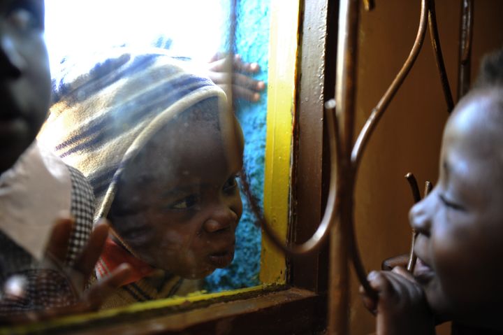 Three-and-a-half year old HIV positive Eugene (C) plays across a window with six-year-old Joan (R) during the last day of classes at their pre-school before their christmas break on December 2, 2010 in Kibera. Eugene, infected with HIV during birth, became an orphan after his mother died when he was a little over one year old and is being raised by his grandmother who is affiliated with the Nyanyo Project who's goal is to empower African grandmothers who care for their grandchildren orphaned by AIDS. Joan also lives with her grandmother after both her parents died of AIDS. Joan is HIV negative. An estimated 22.5 million people are living with HIV in the region - around two thirds of the global total. In 2009 around 1.3 million people died from AIDS in sub-Saharan Africa and 1.8 million people became infected with HIV. Since the beginning of the epidemic 14.8 million children have lost one or both parents to HIV/AIDS. AFP PHOTO / ROBERTO SCHMIDT (Photo credit should read ROBERTO SCHMIDT/AFP/Getty Images)