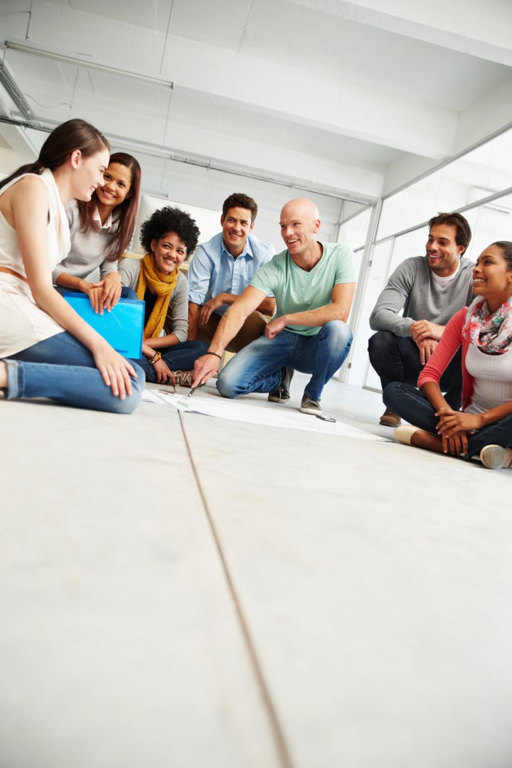 Shot of a large group of positive-looking young designers kneeling on the floor looking at blueprints