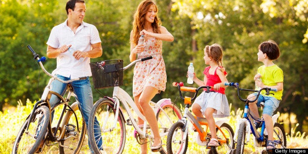 Young happy family riding bicycles outdoors in a park or nature. Making a break to refresh with water. Selective focus to lit