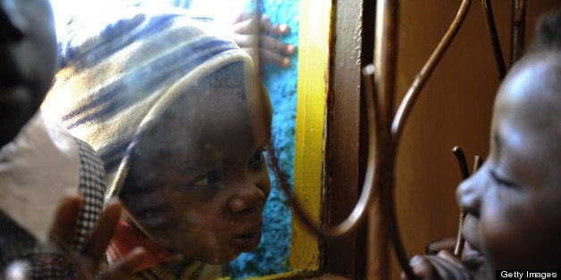 Three-and-a-half year old HIV positive Eugene (C) plays across a window with six-year-old Joan (R) during the last day of classes at their pre-school before their christmas break on December 2, 2010 in Kibera. Eugene, infected with HIV during birth, became an orphan after his mother died when he was a little over one year old and is being raised by his grandmother who is affiliated with the Nyanyo Project who's goal is to empower African grandmothers who care for their grandchildren orphaned by AIDS. Joan also lives with her grandmother after both her parents died of AIDS. Joan is HIV negative. An estimated 22.5 million people are living with HIV in the region - around two thirds of the global total. In 2009 around 1.3 million people died from AIDS in sub-Saharan Africa and 1.8 million people became infected with HIV. Since the beginning of the epidemic 14.8 million children have lost one or both parents to HIV/AIDS. AFP PHOTO / ROBERTO SCHMIDT (Photo credit should read ROBERTO SCHMIDT/AFP/Getty Images)