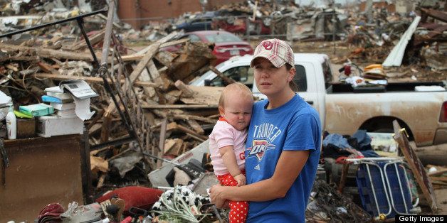 MOORE, OK - MAY 24: Rebecca Smith holds her daughter Ashley while she looks over damage to her parent's home after it was destroyed by a tornado on May 24, 2013 in Moore, Oklahoma. The home is across the street from the Plaza Towers Elementary School (rear) were seven children died in the storm. A two-mile wide EF5 tornado touched down in Moore May 20 killing at least 24 people and leaving behind extensive damage to homes and businesses. U.S. President Barack Obama promised federal aid to supplement state and local recovery efforts. (Photo by Scott Olson/Getty Images)