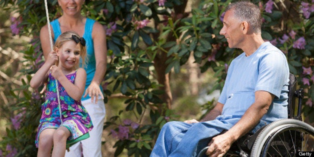 Man with spinal cord injury in wheelchair watching his daughter on swing along with wife