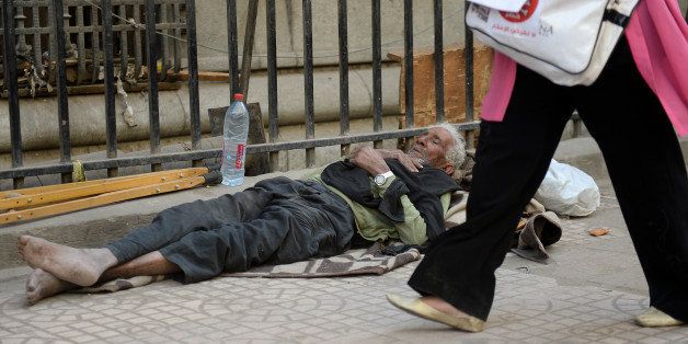 An Egyptian woman walks past a homeless man sleeping on a sidewalk during a rally in downtown Cairo against the visit of a delegation from the International Monetary Fund (IMF) on April 3, 2013. An IMF delegation is in Cairo for talks on a financing programme needed to lift Egypt's economy out of crisis. The government has been walking a tight rope, as the reforms required by the international lender are likely to spark social tensions. AFP PHOTO / KHALED DESOUKI (Photo credit should read KHALED DESOUKI/AFP/Getty Images)