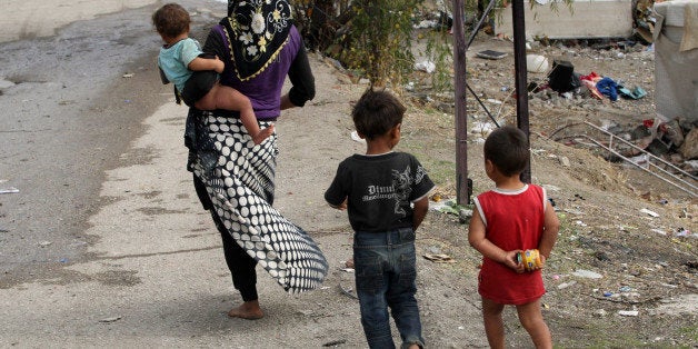 A Syrian refugee woman and children walk near their makeshift tents in central Ankara on October 12, 2013. AFP PHOTO/ADEM ALTAN (Photo credit should read ADEM ALTAN/AFP/Getty Images)