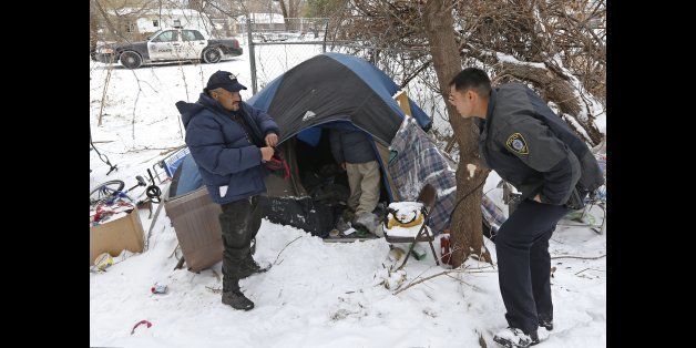 Jack Fontenot, left, puts on his gloves after coming out of a tent at a homeless encampment in Oklahoma City, Friday, Dec. 6, 2013, as Officer Charles McMackin, right, one of Oklahoma City police officers who said they had received complaints about the encampment, waits for the rest of the occupants to emerge. (AP Photo/Sue Ogrocki)