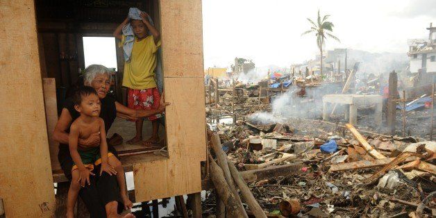 Philippines-weather-typhoon-hope,FOCUS by Karl MALAKUNASTrinidad Genario, 81, sits inside her newly constructed house with her grandchildren, among debris of destroyed houses in Tacloban, Leyte province on December 7, 2013. A raggedy cloth banner in a Philippine town torn apart by one of the most powerful typhoons on record declares that its residents are 'roofless, homeless, but not hopeless'. Super Typhoon Haiyan left more than 7,500 people dead or missing and ruined the homes of about four million others when it tore across some of the Philippines' poorest fishing and farming communities. AFP PHOTO/NOEL CELIS (Photo credit should read NOEL CELIS/AFP/Getty Images)