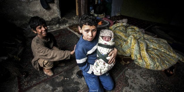 A Syrian refugee boy poses with his newborn brother as their mother lies near them in a house in the Basaksehir district of Istanbul, on March 4, 2014. Syrian government forces are waging a campaign of siege warfare and starvation against civilians as part of its military strategy, a UN-mandated probe said on March 5. Syria's war has since March 2011 killed more than 140,000 people and forced millions more to flee. AFP PHOTO / GURCAN OZTURK (Photo credit should read GURCAN OZTURK/AFP/Getty Images)