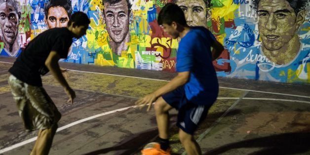 Youngsters play with a football next to a mural with the portraits of famous football players at Tavares Bastos shatytown (favela) in Rio de Janeiro, Brazil, on May 21, 2014. AFP PHOTO / YASUYOSHI CHIBA (Photo credit should read YASUYOSHI CHIBA/AFP/Getty Images)