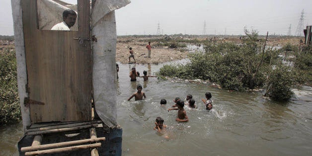 MUMBAI, INDIA: A slum resident uses a toilet that opens into the water below as children swim in the water near a protest rally against the government for demolishing make-shift huts at Mandala in Mankhurd in north central Mumbai, 12 May 2006. In a demolition drive conducted on 09 May 2006, the workers of Brihanmumbai Municipal Corporation (BMC) razed hundreds of hutments during which two girls and three women were rushed to hospital with burn injuries. The mass removal plan is part of a project to shift 200,000 families out of the city's slums into tenement blocks within the next three years, despite protests over tactics employed by officials and police. AFP PHOTO/Sebastian D'SOUZA (Photo credit should read SEBASTIAN D'SOUZA/AFP/Getty Images)