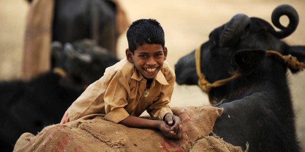 A young boy smiles at the photographer as unseen women sort dried cow dung cakes in the Teliarganj area on the outskirts of Allahabad on December 21, 2009. Cow dung cakes are a major source of domestic fuel for rural households and an environment friendly alternative to firewood in the village areas in many parts of India. In recent times, dung is collected and used as biogas which is used to generate electricity and heat. The gas is a rich source of methane and is used in rural areas of India to provide a renewable, stable and environment friendly source of electricity. AFP PHOTO/Diptendu DUTTA (Photo credit should read DIPTENDU DUTTA/AFP/Getty Images)