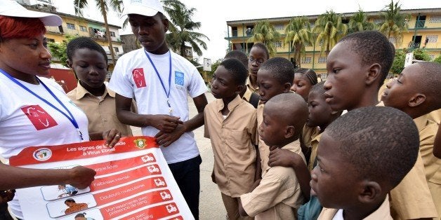 Volunteers wearing t-shirts of the United Nations Development Programme (UNDP) show a placard to raise awareness on the symptoms of the Ebola virus to students of the Sainte Therese school, in the Koumassi district, in Abidjan, on September 15, 2014, on the first day of the school year. The worst-ever Ebola contagion has killed more than 2,400 people in west Africa since it erupted earlier this year and aid agencies deplore an inadequate international response to an emergency that shows no sign of abating. AFP PHOTO / SIA KAMBOU (Photo credit should read SIA KAMBOU/AFP/Getty Images)