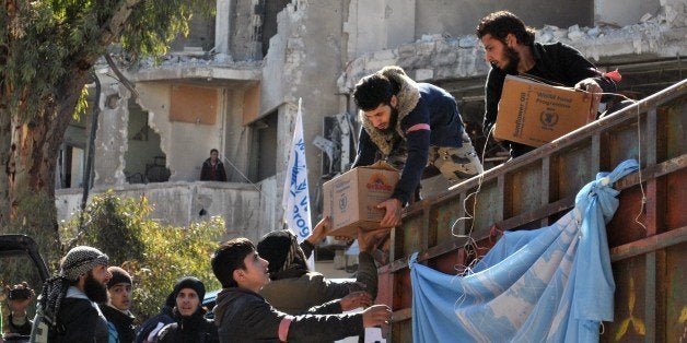Rebel fighters help unload aid food during a UN-led humanitarian operation in the besieged Syrian city of Homs on February 12