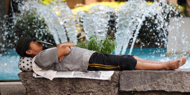 A homeless man takes a nap in front of a fountain at a park in Tokyo, Thursday, July 26, 2012. (AP Photo/Shizuo Kambayashi)