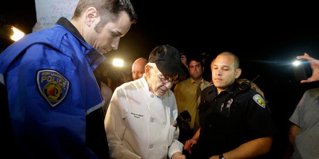 Homeless advocate Arnold Abbott, 90, of the nonprofit group Love Thy Neighbor Inc., center, gets his drivers license to hand to a Fort Lauderdale police officer, Wednesday, Nov. 5, 2014, in Fort Lauderdale, Fla. Abbott and a group of volunteers were feeding the homeless in a public parking lot next to the beach when he was issued a summons to appear in court for violating an ordinance that limits where charitable groups can feed the homeless on public property. Abbott w also recently arrested along with two pastors for feeding the homeless in a Fort Lauderdale park. (AP Photo/Lynne Sladky)