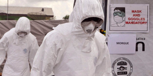 Health workers wearing Ebola protective gear remove the body of a man that they suspect died from the Ebola virus, at a USAID