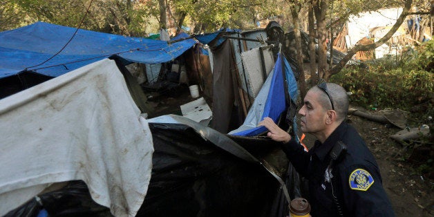 San Jose police officer Eduardo Sandoval looks inside a makeshift tent as notices to move are handed out at the Silicon Valley homeless encampment known as The Jungle, Monday, Dec. 1, 2014, in San Jose, Calif. City officials began posting notices on hand built structures, tents and tree trunks warning the 200 residents of what is likely the nation's largest homeless encampment that the bulldozers are coming. People living in the Silicon Valley camp must be out by Thursday, Dec. 4 or face arrest for trespassing. (AP Photo/Marcio Jose Sanchez)