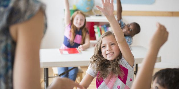 Children (8-9) raising hands in classroom