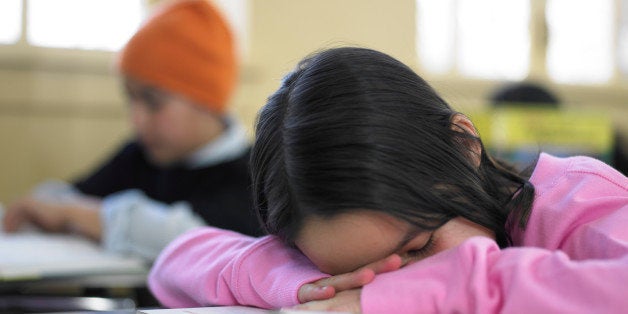 Girl (9-11) resting head on desk in classroom, eyes