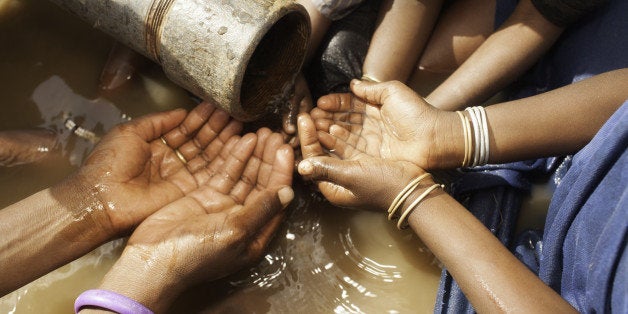 An East African mother and her children gather around a water pipe for drinking. The water in the pipe comes from a concrete water storage tank that was built by an NGO.