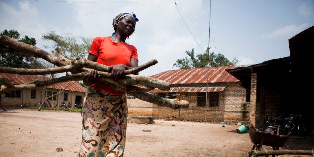 African woman carrying firewood in a backyard.