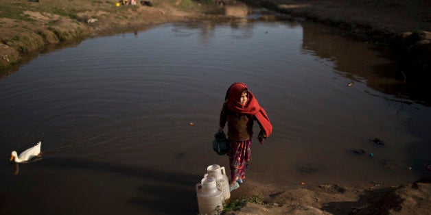 An Afghan refugee child collects water from a polluted stream to be used by her father to fix the walls of their mud home on the outskirts of Islamabad, Pakistan, Monday, Feb. 9, 2015. (AP Photo/Muhammed Muheisen)