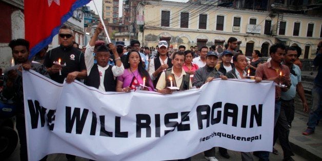 Nepalese people pay tributes to the victims of the April 25 earthquake, as they hold lighted candles near the destroyed landm