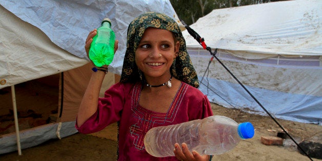 A girl displaced by floods smiles as she carries bottles of drinking water at a camp near Mirpur Khas, in Pakistan's Sindh pr