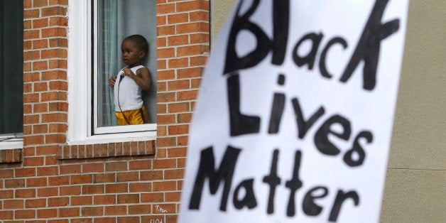 A child watches a protest march for Freddie Gray as it passes by, Wednesday, April 22, 2015, in Baltimore. Gray died from spinal injuries about a week after he was arrested and transported in a police van. (AP Photo/Patrick Semansky)