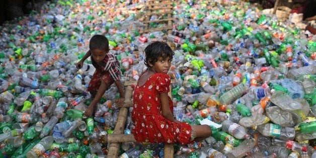 Bangladeshi girl Sharmin, 13 years old, looks into the camera as she works at a plastic recycling factory as a boy plays on a heap of bottles in Dhaka, Bangladesh, Thursday, June 12, 2014. June 12 marks the âWorld Day Against Child Laborâ, that was initiated in 2002 by the International Labor Organization to highlight the plight of child workers across the world. (AP Photo/ A.M. Ahad)