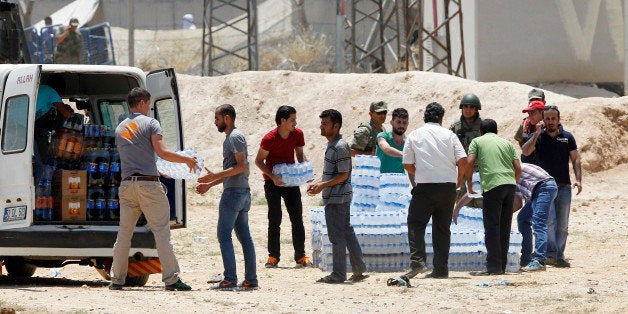 SANLIURFA, TURKEY - JUNE 15: Turkish aid workers carry bottles of water to the the Syrian refugees in Akcakale, on June 15, 2015 in Sanliurfa province, southeastern Turkey. Thousands of Syrians cut through a border fence and crossed over into Turkey on Sunday, fleeing intense fighting in northern Syria between Kurdish fighters and jihadis. The flow of refugees came as Syrian Kurdish fighters closed in on the outskirts of a strategic Islamic State-held town on the Turkish border, Kurdish officials and an activist group said, potentially cutting off a key supply line for the extremists' nearby de facto capital. According to Turkish security officials 10,000 people to come across from Syria in last two days. (Photo by Gokhan Sahin/Getty Images)