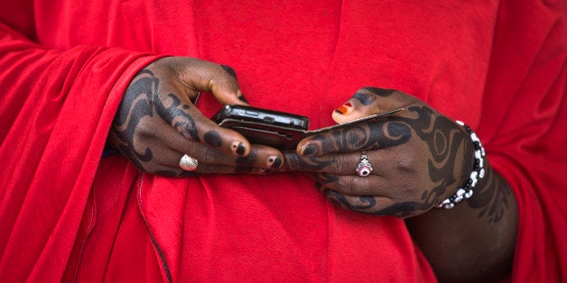 A woman from the Hausa tribe, with a red mark on her thumbnail indicating she has already validated her voting card, looks at her smartphone while she waits for friends to finish the process, at a polling station located in an Islamic school in Daura, the home town of opposition candidate Gen. Muhammadu Buhari, in northern Nigeria Saturday, March 28, 2015. Nigerians went to the polls Saturday in presidential elections which analysts say will be the most tightly contested in the history of Africa's richest nation and its largest democracy. (AP Photo/Ben Curtis)