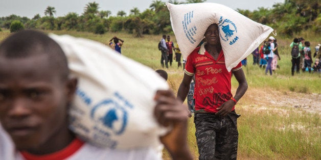 People carry food aid from a British Navy helicopter after it made a food drop on Sherbro Island, Sierra Leone, Sunday, Dec. 7, 2014. The WFP, World Food Program and British Military took part in a three day food distribution effort to local residents on the remote Sherbro Island, where the amount of sick people due to the Ebola virus have prevented people from farming, fishing or gathering there own food. (AP Photo/Michael Duff)