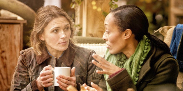Two female friends discussing over a cup of coffee. They are sitting outdoors in Autumn. Halloween pumpkins can be seen in th