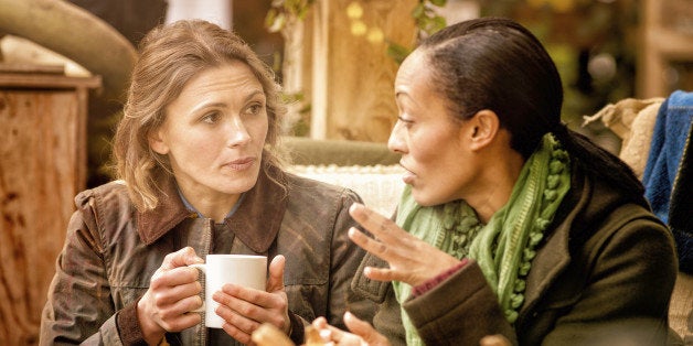 Two female friends discussing over a cup of coffee. They are sitting outdoors in Autumn. Halloween pumpkins can be seen in the foreground.