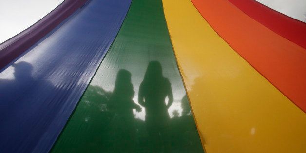 A LGBT (Lesbians Gays Bisexuals and Transgenders) couple is silhouetted by their rainbow-colored symbol while waiting to march around the University of the Philippines campus in an annual event to draw the attention to their issues as gay rights and anti-discrimination Friday, Sept. 11, 2015 at suburban Quezon city northeast of Manila, Philippines. More than a hundred LGBTs joined the march which culminated in a concert.(AP Photo/Bullit Marquez)
