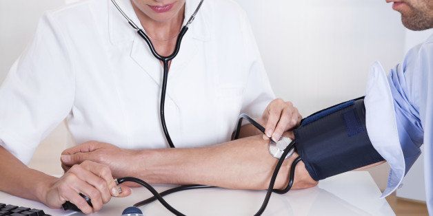 Attractive young female doctor or nurse taking a male patients blood pressure using a sphygmomanometer