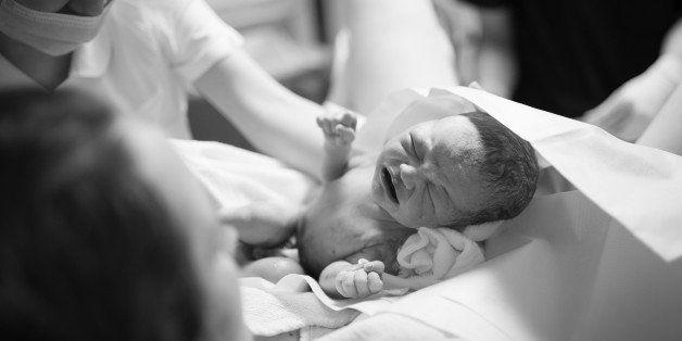 Black and white image of the moment a newborn is delivered, with mother, midwife and baby.