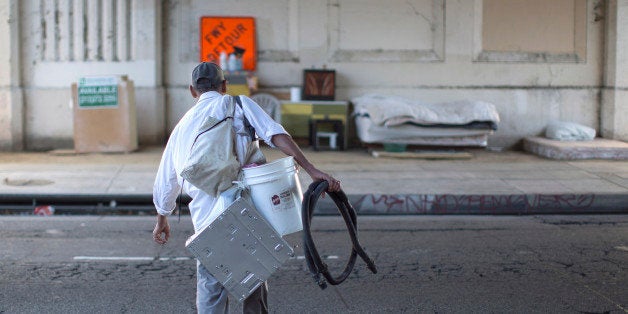 LOS ANGELES, CA - NOVEMBER 20: Fernando Lopez carries possessions to his street side encampment which is protected from mino