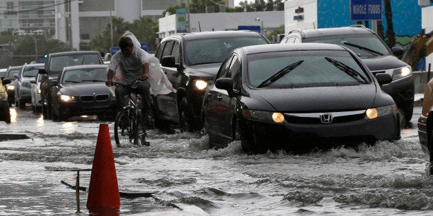 A cyclist and vehicles negotiate heavily flooded streets as rain falls, Tuesday, Sept. 23, 2014, in Miami Beach, Fla. Certain