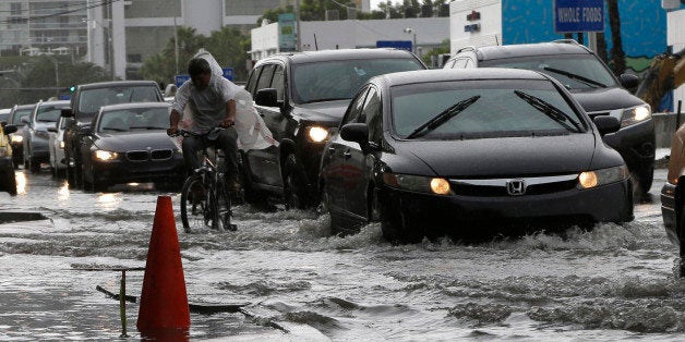 A cyclist and vehicles negotiate heavily flooded streets as rain falls, Tuesday, Sept. 23, 2014, in Miami Beach, Fla. Certain neighborhoods regularly experience flooding during heavy rains and extreme high tides. New storm water pumps are currently being installed along the bay front in Miami Beach. National and regional climate change risk assessments have used the flooding to illustrate the Miami area's vulnerability to rising sea levels. (AP Photo/Lynne Sladky)