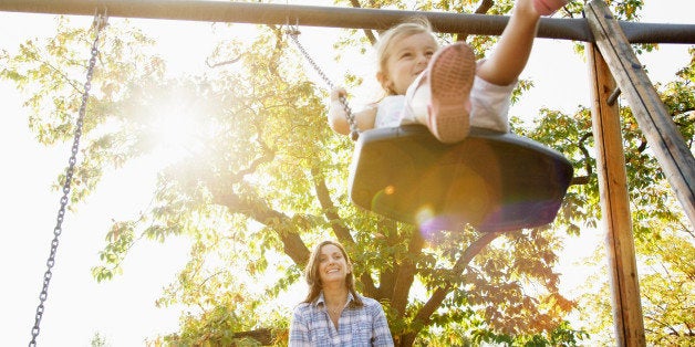 Mother pushing daughter on swing in sunny park