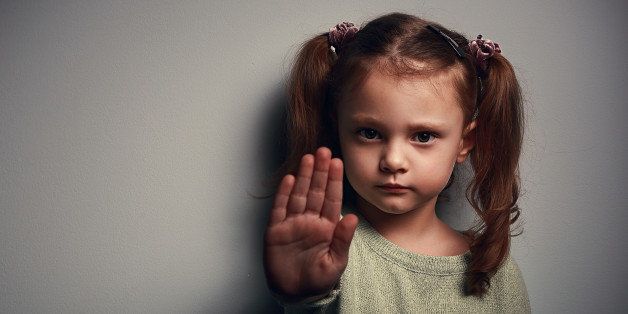 Angry kid girl showing hand signaling to stop useful to campaign against violence and pain on dark background. Closeup portrait