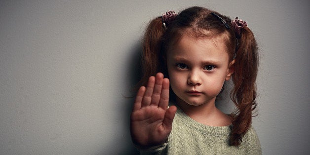 Angry kid girl showing hand signaling to stop useful to campaign against violence and pain on dark background. Closeup portra