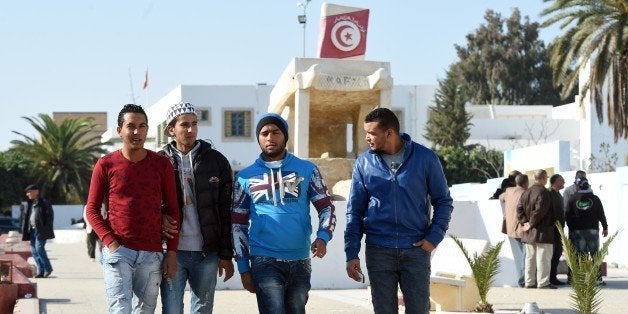 Tunisian graduates and unemployed youth walk on Mohamed Bouazizi square on December 14, 2015, in the impoverished central town of Sidi Bouzid, three days ahead of the fifth anniversary of the self-immolation of Mohamed Bouazizi, a young street vendor, which sparked the revolution that ousted a dictator and ignited the Arab Spring. Five years after triggering the Arab Spring, Tunisians doggedly pursue a democratic transition while other countries remain gripped by violence and repression. In the background is a sculpture erected after Bouazizi's death featuring a barrow and symbolising poverty. AFP PHOTO / FETHI BELAID / AFP / FETHI BELAID (Photo credit should read FETHI BELAID/AFP/Getty Images)