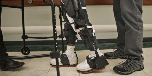 James Cody, 29, center, walks with the aid of a bionic exoskeleton and physical therapists at the Burke Rehabilitation Center in White Plains, N.Y., Monday, Nov. 10, 2014. Cody suffered a traumatic brain injury during a car accident in 2011 and has been doing multiple therapies, including using this bionic exoskeleton, to improve his health. (AP Photo/Seth Wenig)