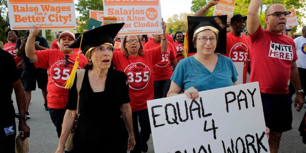 A woman carries a sign for equal pay as she marches with other protestors in support of raising the minimum wage to $15 an ho